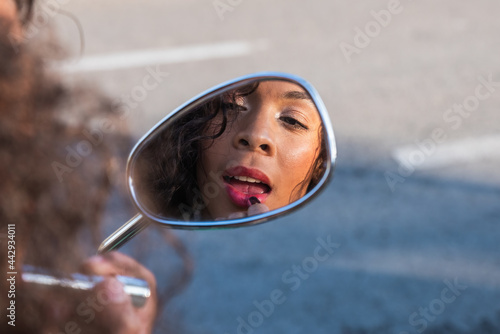 Wistful ethnic woman rouging lips in scooter mirror photo