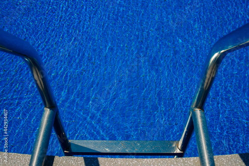 Steps to the pool, blue clear water in the outdoor swimming pool, safe descent to the pool, close-up steps through the water