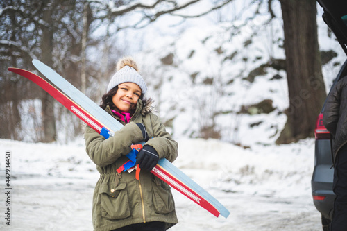 Porträtt av leende flicka som bär skidor stående vid bil utomhus photo