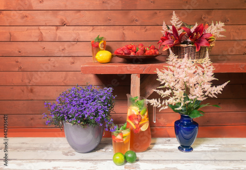 Lemonade, plate of strawberry, wicker basket with beautiful red lilies and pink astilbe flowers, pink astilbe flowers in blue vase and lobelia blue blossom in flower pot.
