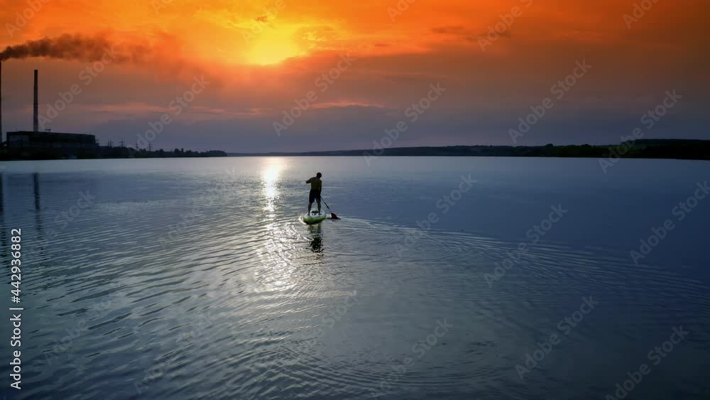 Man sailing on river. Sports training on water against beautiful sunset. Athlete is rowing on the evening water while standing with an oar. Water sports. Man sailing on river. Sports training on water against beautiful sunset. Athlete is rowing on the evening water while standing with an oar. Water sports.