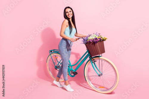 Full length body size photo woman riding retro bike in summer with flowers isolated pastel pink color background © deagreez