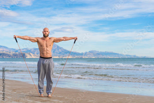 Focused bearded man working out with elastic bands on coast photo