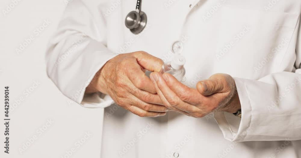 An elderly doctor wearing a white apron, holding a hand sanitizer, antibacterial gel, dispenses the liquid on his hands and rubs it into mature hands, takes care of hygiene, puts it in his pocket An elderly doctor wearing a white apron, holding a hand sanitizer, antibacterial gel, dispenses the liquid on his hands and rubs it into mature hands, takes care of hygiene, puts it in his pocket