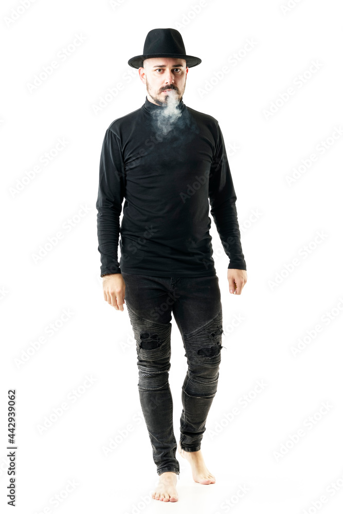 Authentic unique style artist in full black clothes and hat walking barefoot and smoking. Full body portrait isolated on white background Authentic unique style artist in full black clothes and hat walking barefoot and smoking. Full body portrait isolated on white background