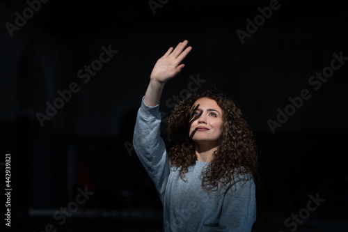 Portrait of young woman standing indoors against black bacground, playing with shadow. © Halfpoint