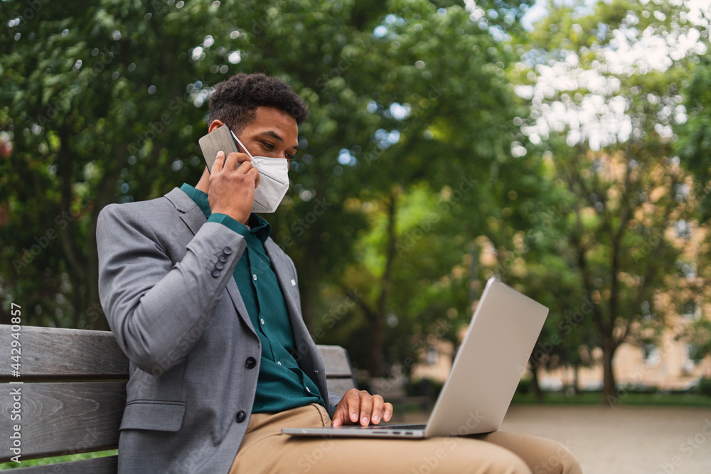 Young man with respirator using laptop and smartphone outdoors in city, covid-19 concept. Young man with respirator using laptop and smartphone outdoors in city, covid-19 concept.