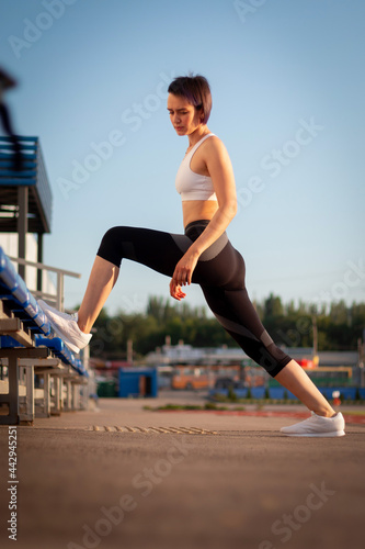 Sport and wellness. Fitness girl in white sneakers doing stretching workout. Fashion sporty woman with strong muscular body training. Fit female stretching at outdoor stadium