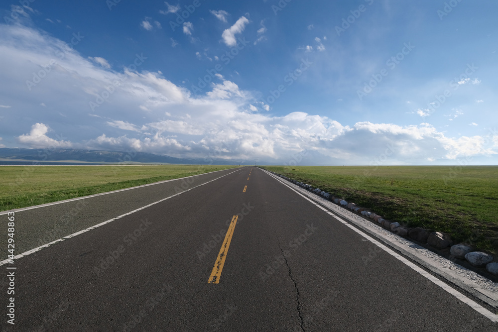 empty asphalt road at grass plain. Wide Horizon and white clouds blue sky. Wide angle