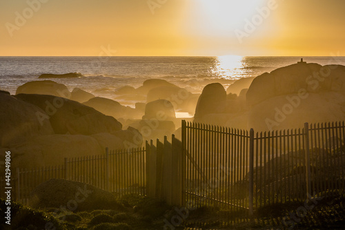 Sunset at Camps Bay. During golden hour, the mist and the waves allow Sun rays to be appreciated and behind a fence. Cape Town, South Africa, Cape of Good Hope. photo