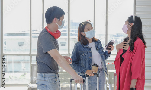 Young asian traveler friend group wearing face mask enjoy chatting together when meets at airport terminal station. COVID-19 new normal travel concept. Selective focus.