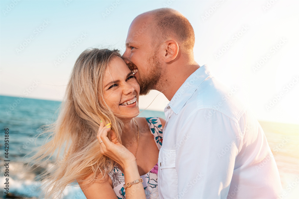 Fototapeta premium A couple of happy young men and women hug and kiss. In the background, the ocean and the sky. Vacation romance concept