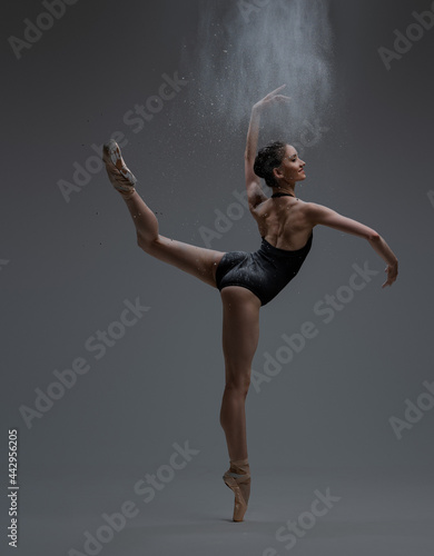 Obraz na plátně Graceful ballerina spraying dust and dancing inside studio