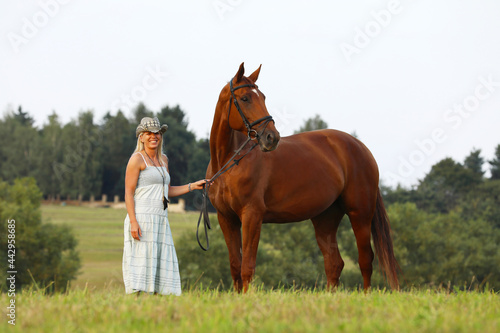 Portrait of a beautiful cheerful woman with cowboy hat and horse outdoors. Meadow in summer day