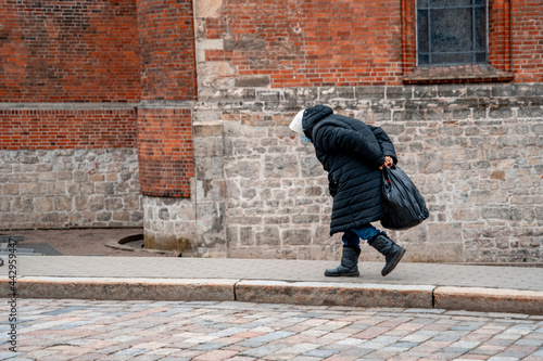 Obraz na płótnie Elderly woman in a blue mask, hunched over, walks down the street (173)