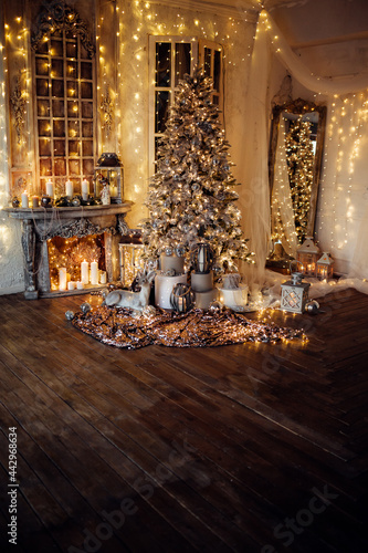 warm and cozy evening in Christmas room interior design,Xmas tree decorated by lights presents gifts,toys, deer,candles, lanterns, garland lighting indoors fireplace.holiday living room.magic New year