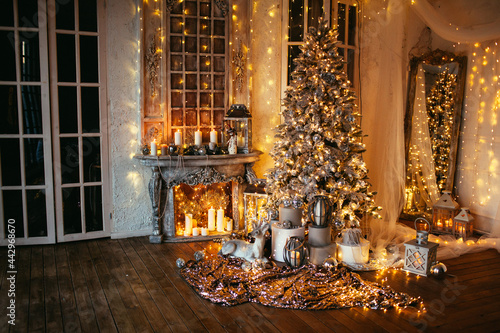 warm and cozy evening in Christmas room interior design,Xmas tree decorated by lights presents gifts,toys, deer,candles, lanterns, garland lighting indoors fireplace.holiday living room.magic New year