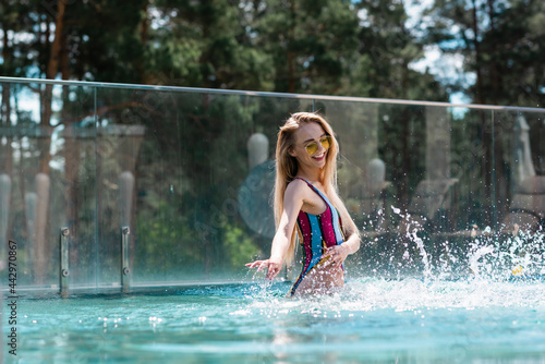 Positive woman splashing water in swimming pool at resort