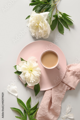 Summer romantic breakfast with coffee cup and white peonies flowers on gray office desk. Feminine workplace, top view, flat lay. photo