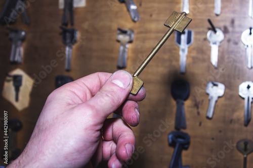 The master holds a long golden key against the background of other blanks for making copies of keys