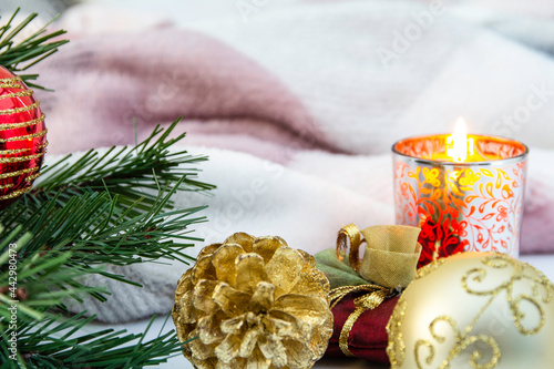 Christmas Theme with a lit Candle, Blanket and Christmas  tree decorations to the foreground