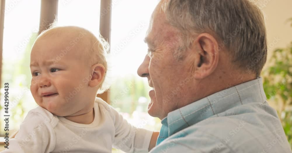 An old man, grandfather holds his grandchild in his arms, looks at him, calms him down, talks to him, tells him a story, the child grimaces, cries, listens, looks around An old man, grandfather holds his grandchild in his arms, looks at him, calms him down, talks to him, tells him a story, the child grimaces, cries, listens, looks around