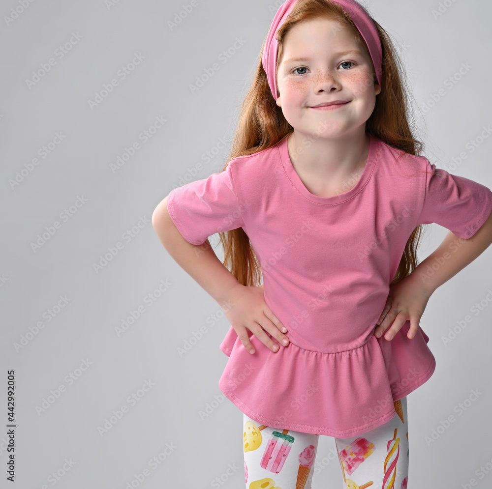 Friendly smiling little red-haired girl wearing summer fashion clothes, looking at the camera. Adorable little female model studio portrait shot. Positive emotions of children Friendly smiling little red-haired girl wearing summer fashion clothes, looking at the camera. Adorable little female model studio portrait shot. Positive emotions of children