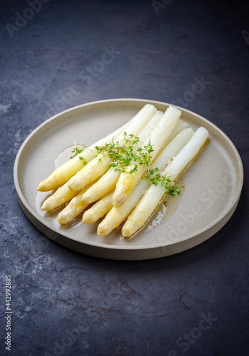 Modern style traditional steamed white asparagus with butter sauce hollandaise and cress served as close-up on a Nordic design plate