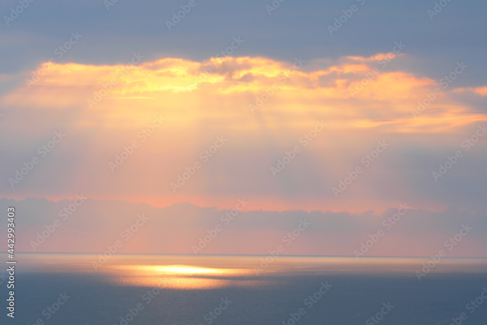 Landscape with sunset on the horizon of the sea and the sky with dramatic clouds and rays of the sun in pink and blue pastel colors.