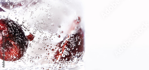 Close-up of a glass with a gin and tonic summer cocktail and cherry halves with ice cubes on white background with copyspace