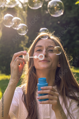 Adorable young woman plays outdoors with soap bubbles. Cute woman relaxes in nature on a sunny day. Weekends concept.