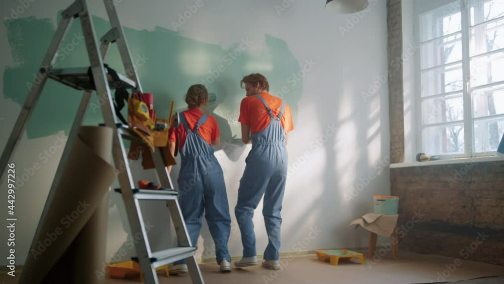 Happy couple painting wall indoors. Family dancing during decoration in home. Happy couple painting wall indoors. Family dancing during decoration in home.