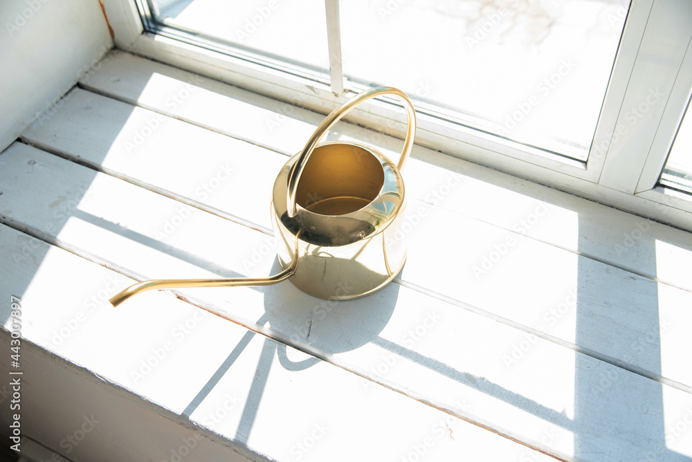 a yellow brass watering can with a long spout on a white windowsill. overexposed frame