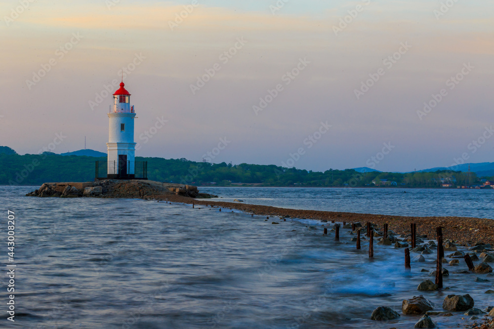 Tokarevsky lighthouse in Vladivostok. Old white lighthouse on the background of the sea and the green island. Marine landmark of the Primorsky region.