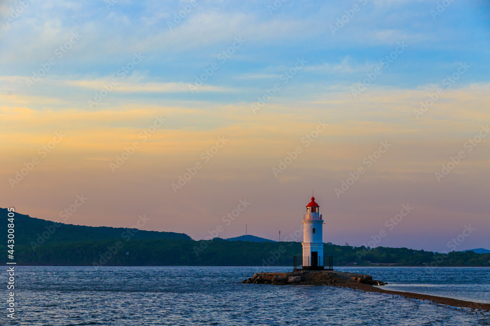 Tokarevsky lighthouse in Vladivostok. Old white lighthouse on the background of the sea and the green island. Marine landmark of the Primorsky region.