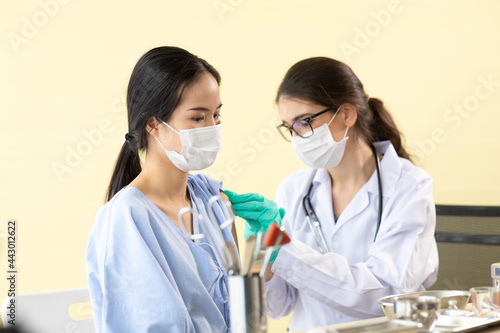 woman doctor holding syringe and injection vaccine shot to patient. Young asian woman sitting and getting vaccinated against coronavirus in hospital