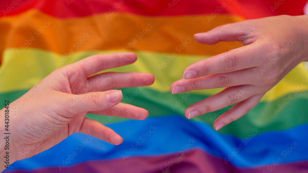 Fototapeta premium Parody of the mural Creation of Adam on the background of the LGBT flag during the celebration of the month of dignity, Bisexuality Day or National Coming Out Day. Female hands of lesbians