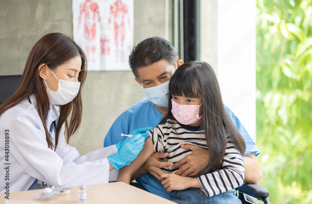 Asian senior doctor wearing gloves and isolation mask is making a COVID-19 vaccination in the shoulder of child patient with her mother at hospital. Asian senior doctor wearing gloves and isolation mask is making a COVID-19 vaccination in the shoulder of child patient with her mother at hospital.