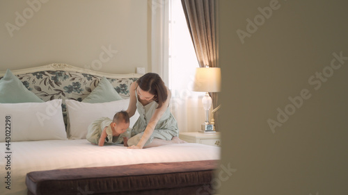 asian woman mother parent encourage baby infant to sit and crawl on soft bed at luxury home. 6 months kid put effort  learning lesson development skill. mom playing with baby infant on bed in bedroom.