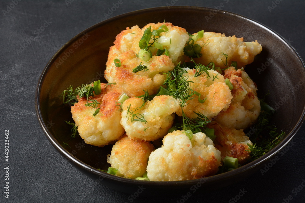 Fried cauliflower florets in batter on a black plate. Coated fried cauliflower Fried cauliflower florets in batter on a black plate. Coated fried cauliflower