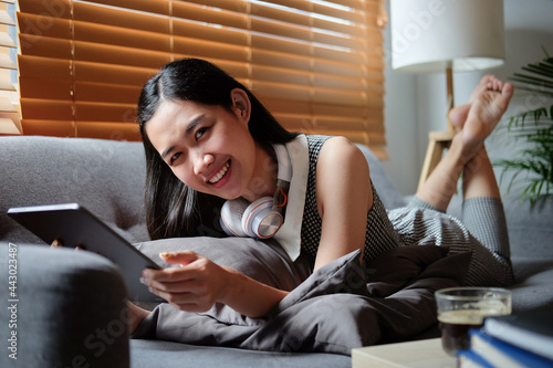 Smiling young woman sitting on comfortable sofa and using digital tablet. 