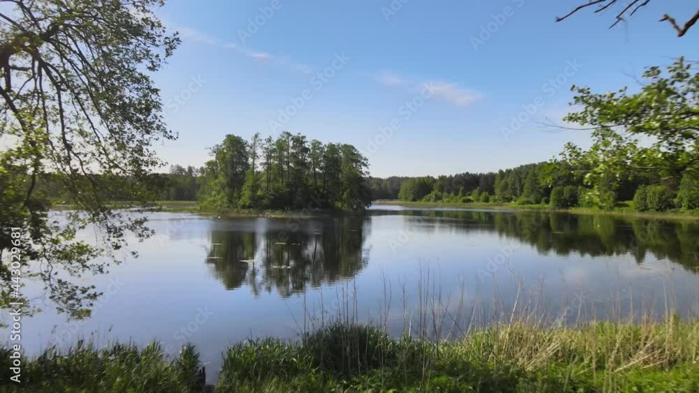 Top view of a lake in the forest with a small island,green trees around and in the midle of the lake water with reflecting sun rays Top view of a lake in the forest with a small island,green trees around and in the midle of the lake water with reflecting sun rays