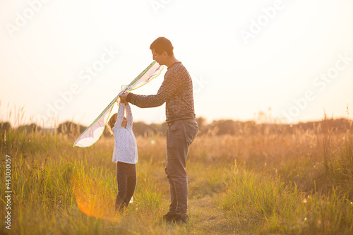 Dad helps his daughter to fly a kite in a field in the summer at sunset. Family entertainment outdoor, Father's Day, Children's Day. Rural areas, support, mutual assistance. Orange light of the sun