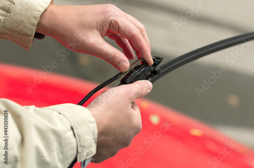 Man snaps a new wiper blade on the holder in the background of a red car