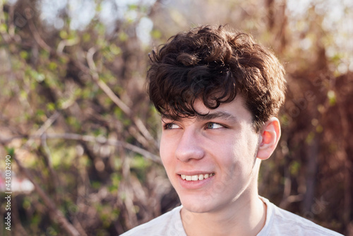 Portrait of a teenage boy close up on a forest background, the guy smiles and looks away, the guy has a positive look, he seems to be looking to the future with faith