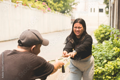 A young asian woman struggles to get her bag back from a devious snatcher. A victim of a thief on the streets. photo