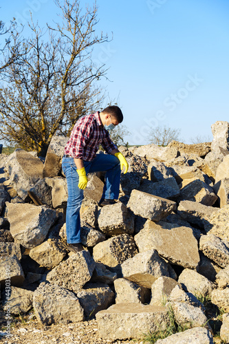 a man works with a pile of stones and broken pieces of concrete, carries construction debris