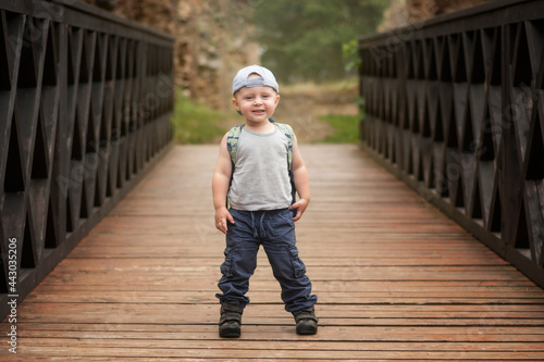 Two year old Caucasian boy in sportswear posing during a trip on a wooden bridge.