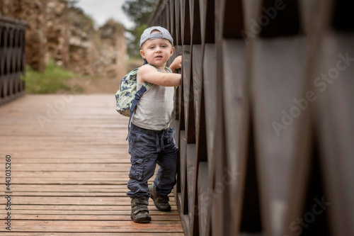 Two year old Caucasian boy posing leaning against a wooden bridge railing.
