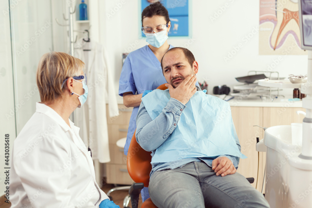 Obraz premium Stomatologist doctor talking to man patient with toothache sitting on dental chair preparing for medical examination. Dentists team working in stomatology hospital clinic office